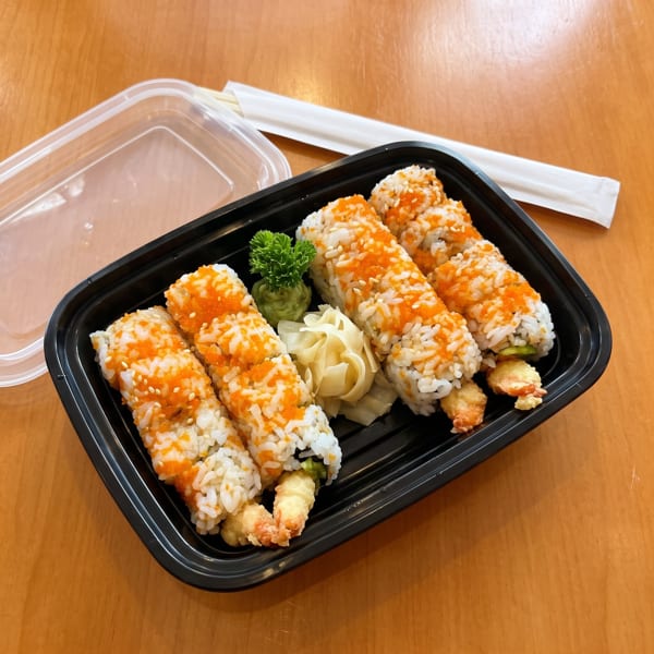 Sushi rolls with orange roe and sesame seeds, ginger, and wasabi in a black takeout container.