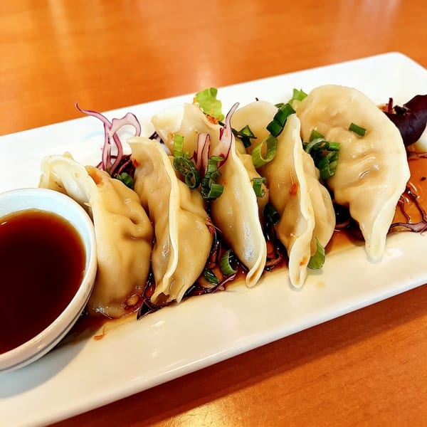 A plate of steamed dumplings with green onions, red cabbage, and a side of soy sauce.
