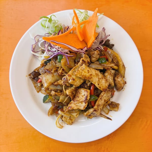 Stir-fried chicken with wide noodles, vegetables, and a carrot garnish on a white plate.