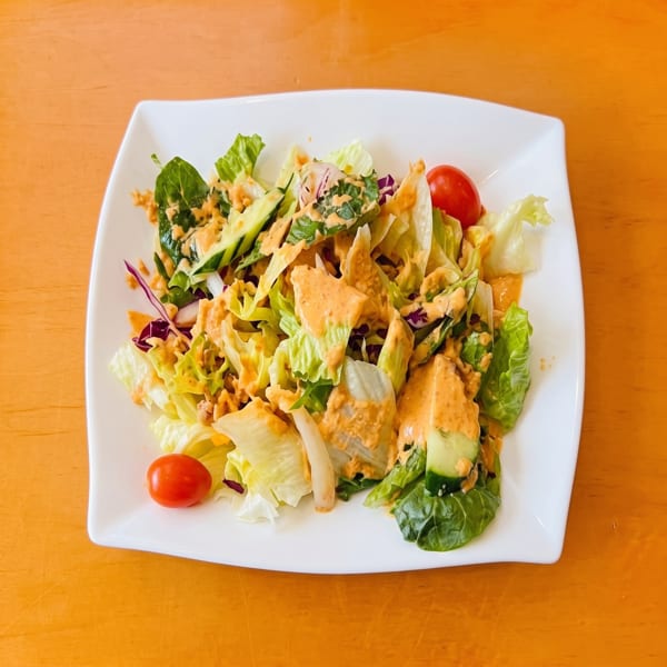 Fresh garden salad with mixed greens, cucumbers, cherry tomatoes, and creamy orange dressing on a white plate.