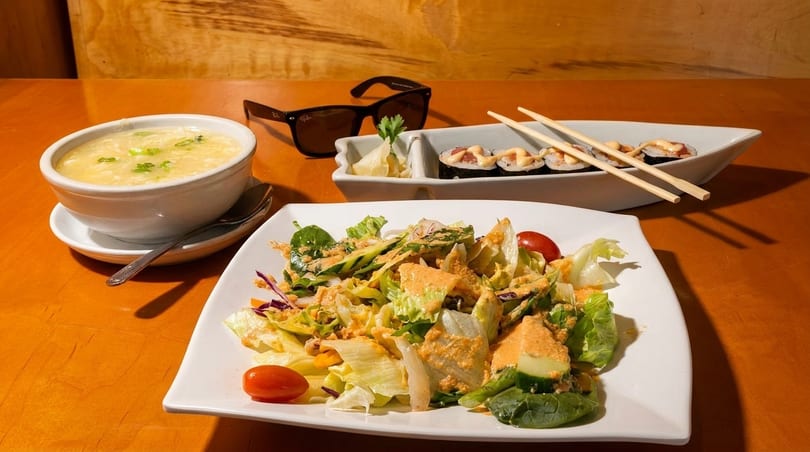 A bowl of egg drop soup, a plate of salad, and a boat-shaped dish of sushi rolls.