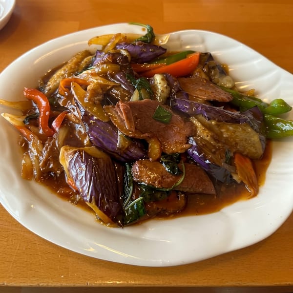 Szechuan eggplant with beef, bell peppers, and onions in a rich brown sauce on a white plate.