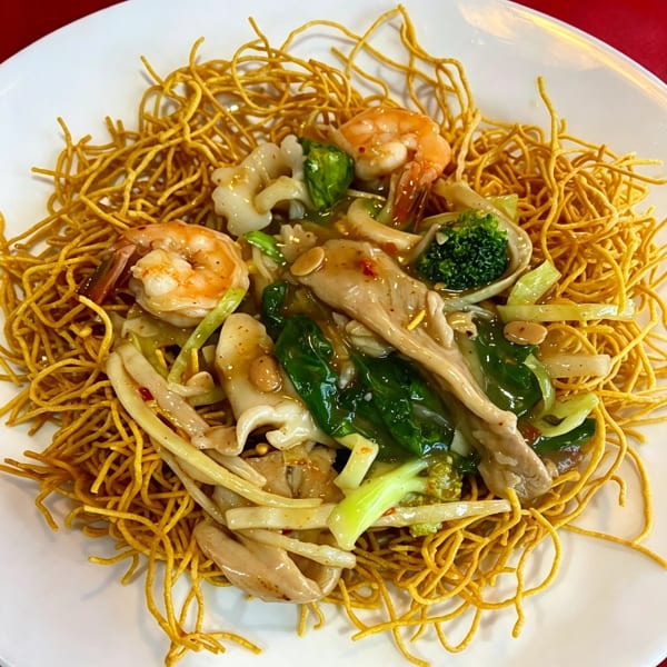 Crispy pan-fried noodles topped with shrimp, squid, broccoli, and leafy greens in a savory sauce.