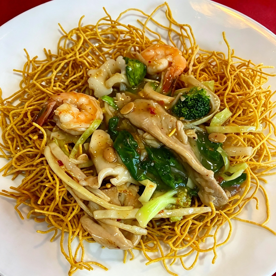 Crispy pan-fried noodles topped with shrimp, squid, broccoli, and leafy greens in a savory sauce.