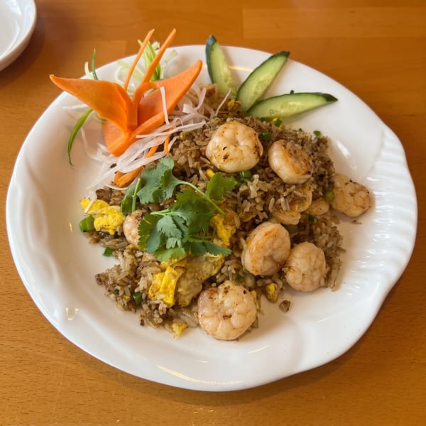 Shrimp fried rice with egg, peas, and cilantro, garnished with carrot and cucumber slices.