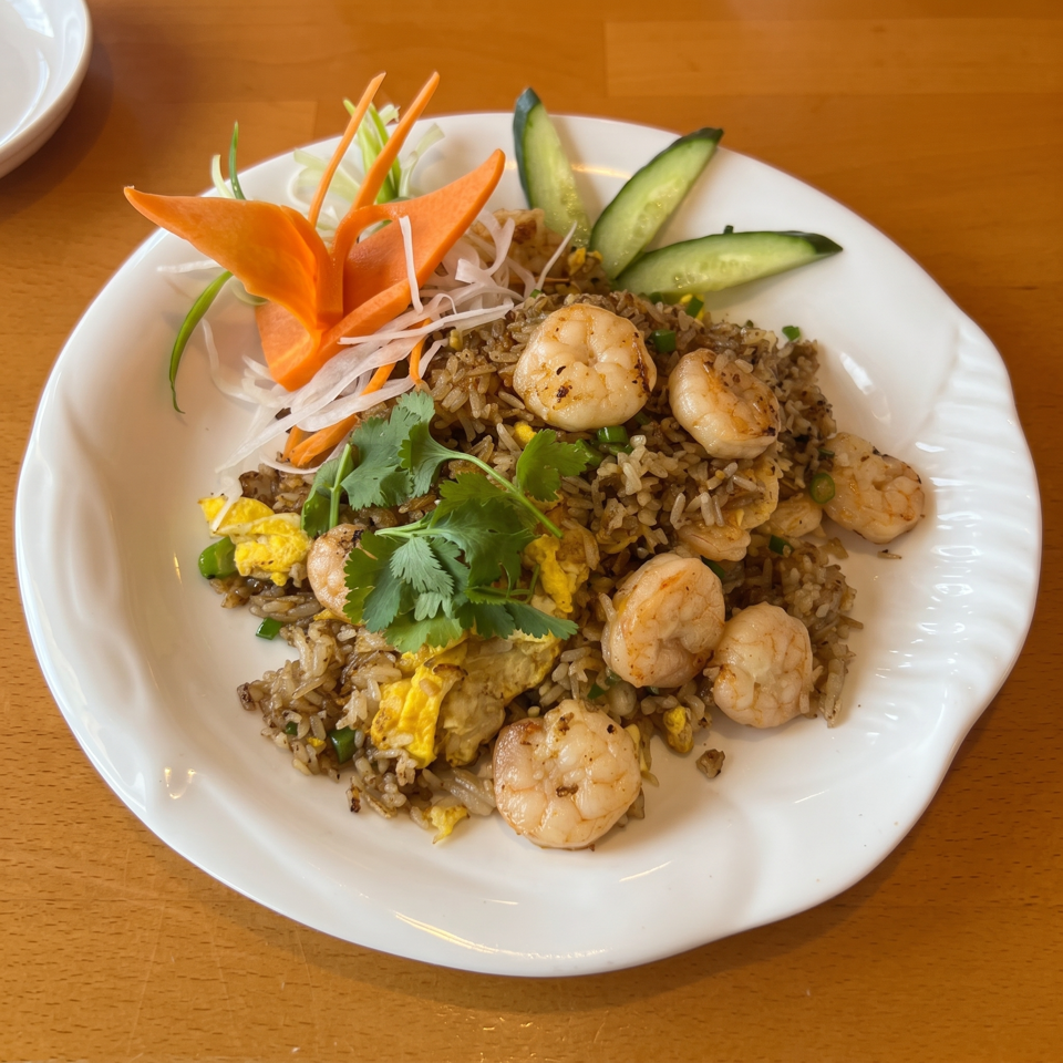 Shrimp fried rice with egg, peas, and cilantro, garnished with carrot and cucumber slices.