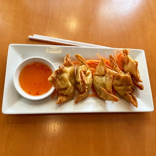 Crispy fried wontons with sweet chili dipping sauce and shredded carrots on a white rectangular plate.